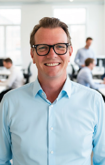 Jeroen van der Geest, lachend in een lichtblauw hemd op een kantoorvloer.
